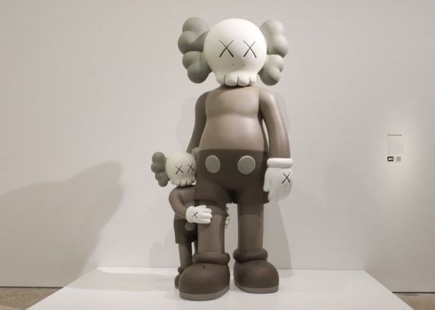 two monotome grey sculptures of characters based loosely on mickey mouse, a parent and a child clinging to parent's knee, title is Good Intentions