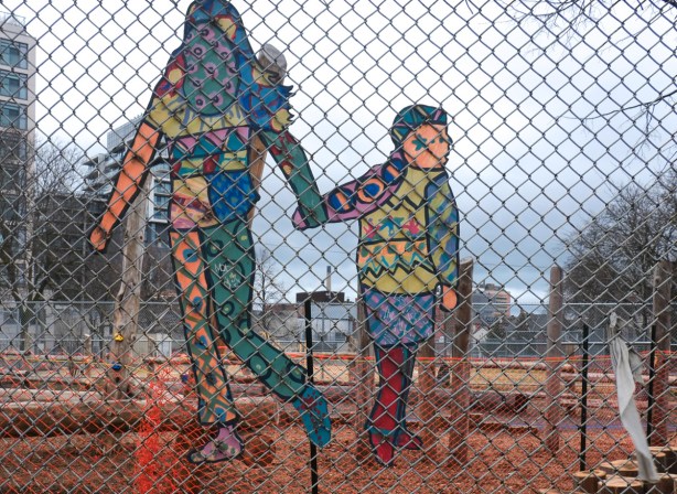 painted cutouts on a chainlink fence around lord lansdowne school, a mother and child holding hands