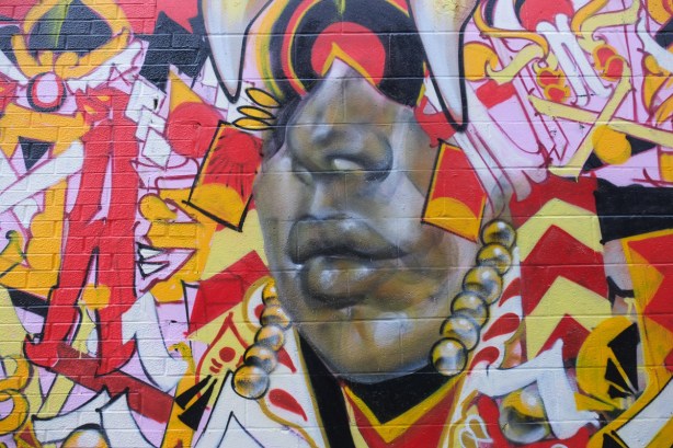 mural by Rowell Soder in an alley, part of a face, mouth and nose, surrounded by red, yellow, and white shapes