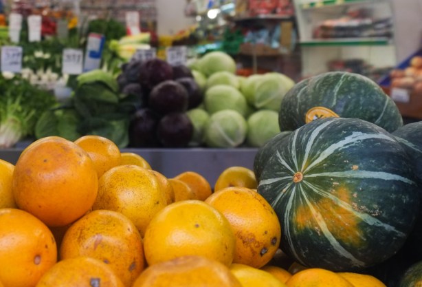 looking in the window of a fruit and vegetable store, large green squash and a pile of oranges beside the window