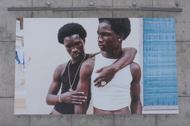 large photograph displayed outside, two Black men, one has his arm around the other