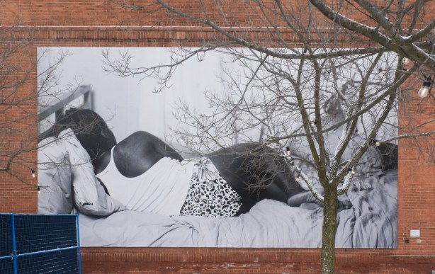 large black and white photo displayed on exterior wall of art gallery, person lying down with back to the camera
