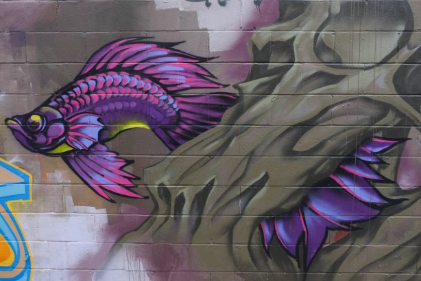 street art mural of a large purple fish with billowy tail, swimming,