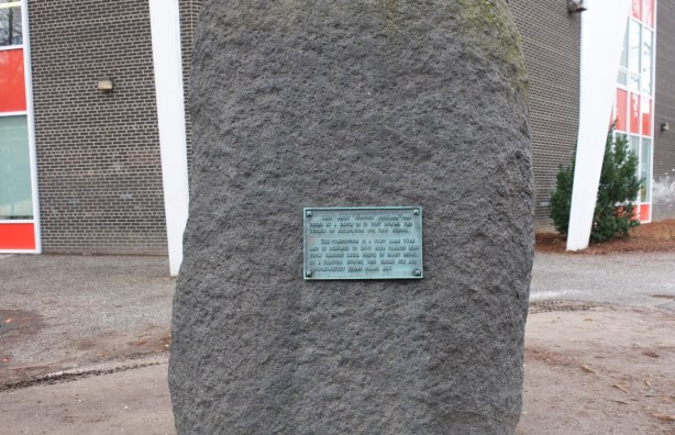 large grey rock in a schoolyard with a plaque on it describing the rock