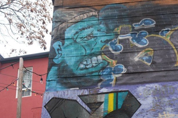 painting of a teal coloured man on a wood fence in a Kensington alley