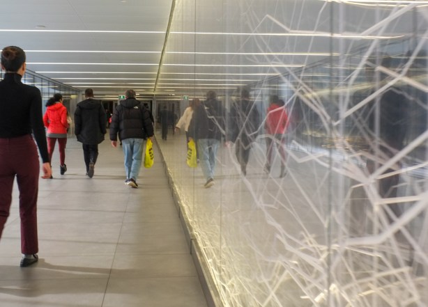 elevated enclosed walkway over street, with one wall made of glass with artwotk of LED lights running through it 