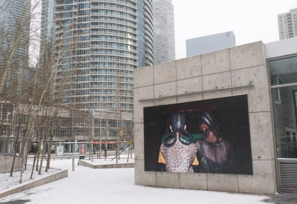 large photo of two Black women with their hair in curved shapes made from braids, displayed outside in winter, Queens Quay, Ontario Square