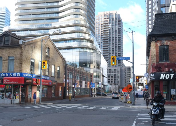 wellesley street looking west from yonge street, convenience store on southwest croner, noew curvy condo tower in glass behind it