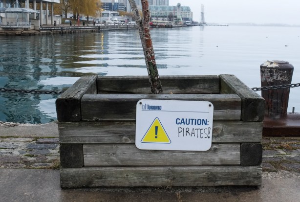 caution sign on a wood tree planter that someone has written the word pirates on, so sign now says caution, pirates!