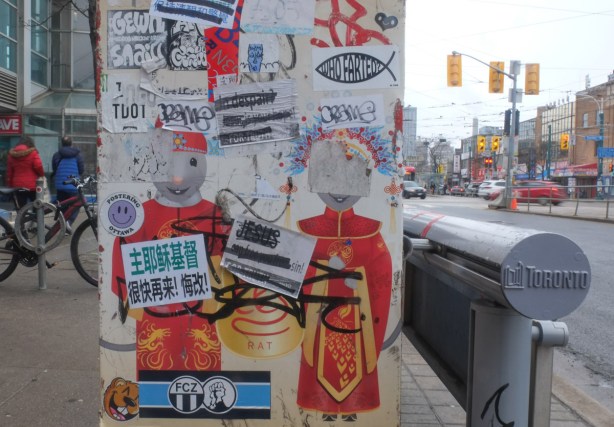 side of a canada post mailbox with chinese characeters, one male and one female, on the side, also stickers and graffiti slaps on it 