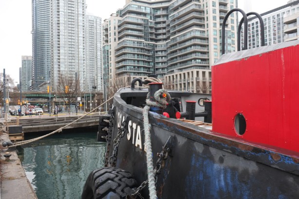 a boat tied up at a dock, with city street scene behind