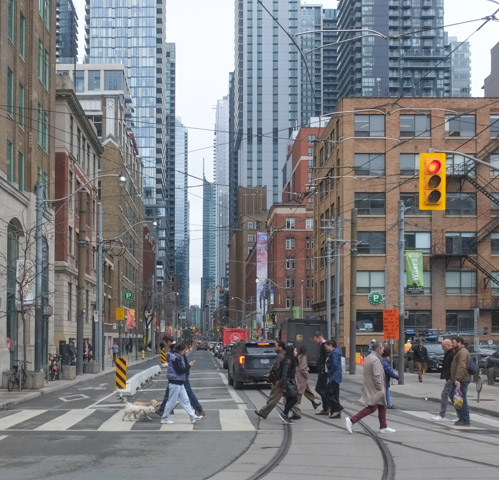 people crossing Adelaide Street at Spadina, looking eastward along Adelaide with Yonge street in the distance, large tall buildings on both sides of adelaide