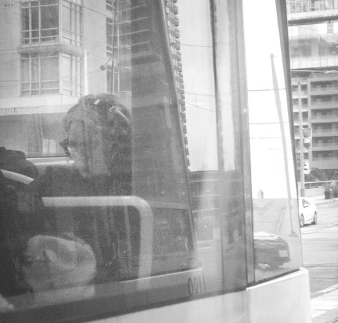 black and white photograph of a woman sitting at the back of a streetcar, looking through the window