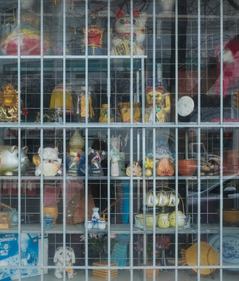 window display of asian chinese store in chinatown on spadina, metal grille in window as well, tea cups, silver piggybank, porcelain figurines, 