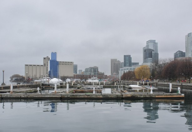 view of Toronto waterfront, looking west from Spadina Quay, towards large Canada Malting Co silos, boats in the foreground, but not many because it's winter, some wrapped in white, foggy grey day