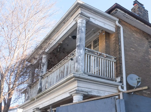 view above the hoardings, abandoned house, upper level, old white balcony, brick house, satelite dish, brick chimney, 