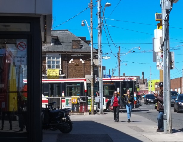 southwest corner of Edna and Dundas West, standing in front of Mcdonalds at the subway station, a bus, some people walking, a man leaning against a telephone pole.