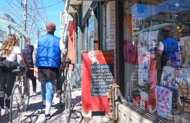 a young man walks his bike on sidewalk past a store, reflections in the window