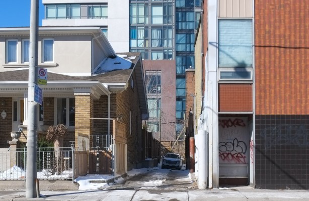 car parked in a driveway beside an older house, with a taller glass and brick condo building behind