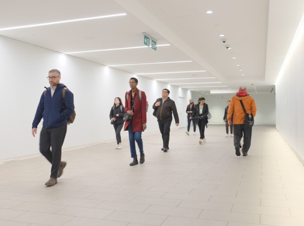 people walking through an all white tunnel connecting to the subway, well lit, 