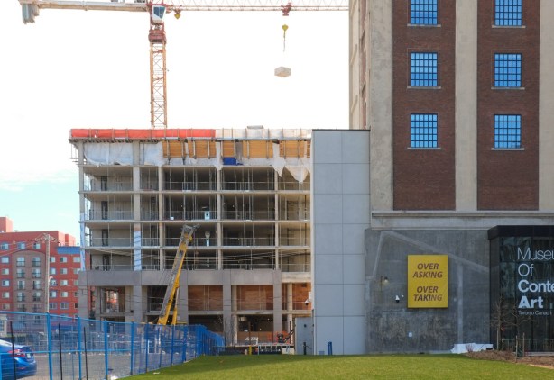 back corner of MOCA, Museum of Contemporary Art, with new construction of a new building beside it, crane on top of new building, sign on the back of MOCA that says over asking under taking