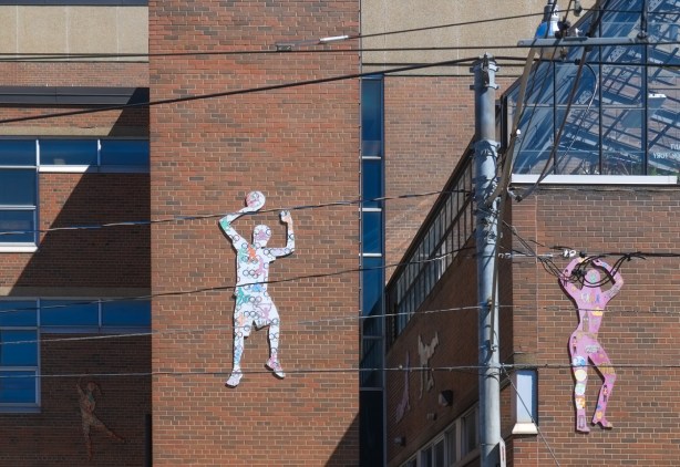 wood cutouts of people doing things, man holding a ball above his head, painted, mounted on exterior of red brick building, a school,