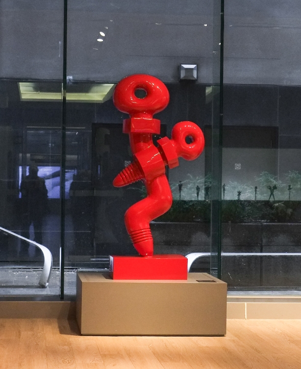 red sculpture in a gallery, human like shape made of two large screws