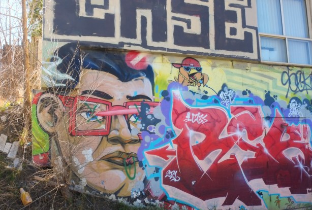 uber 5000 mural in an alley, a yellow bird in a red cap, a man with square red framed glasses