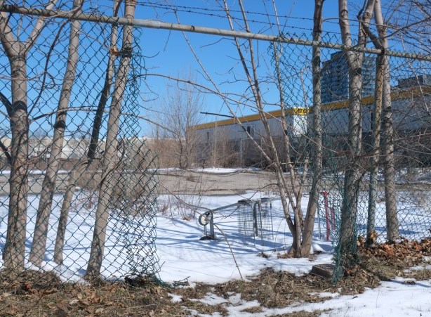 empty metal shopping cart lying on its side on the other side of a chain kink fence with a large hole in it, ground covered with snow