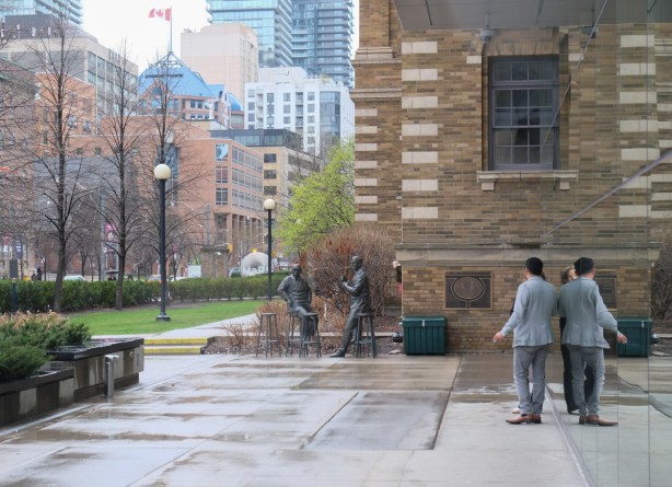 outside mars building on college street, two people are talking, also two bronze statues, buildings on college street