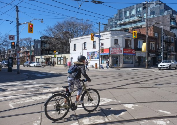 a person on a bike riding north on Roncesvalles, past Whites Corner Variety