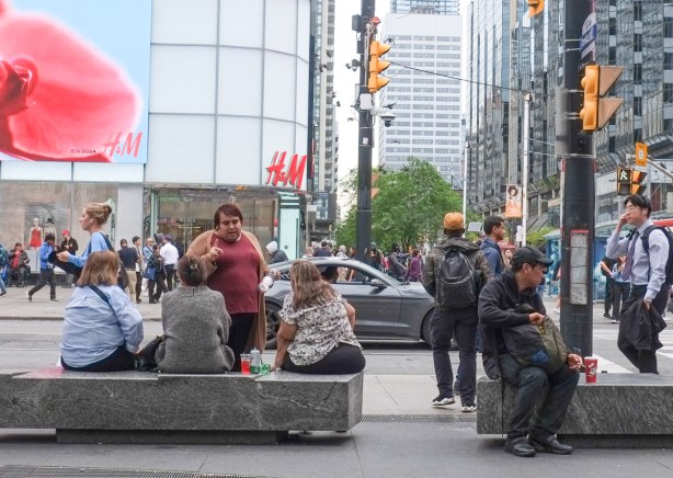 group of people sitting on a bench at Yonge Dundas square, others standing or walking nearby