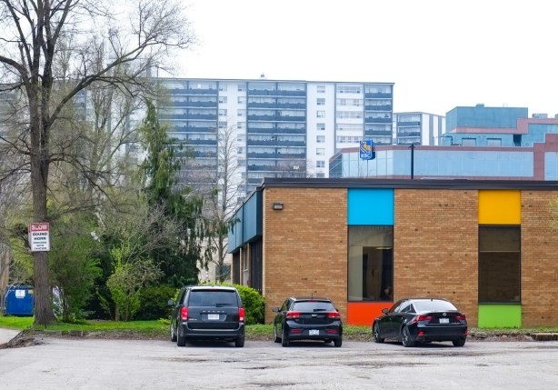 back of a light industrial building that is red brick with large sections of coloured trim, parking lot, apartment building on Thorncliffe in the background