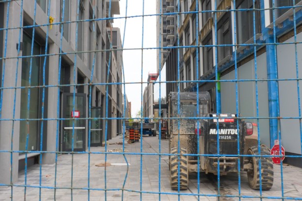 behind blue construction fence, machinery, two tall condo being built with laneway between them