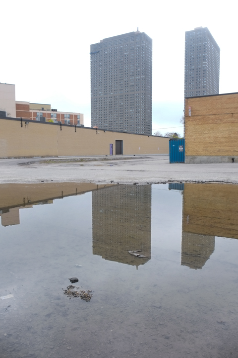 large puddle reflects a couple of high rise office buildings as well as a low brick warehouse building