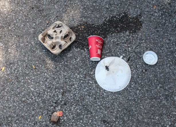 a tims coffee cup on the ground beside a cardboard take out drinks tray and a plastic plate