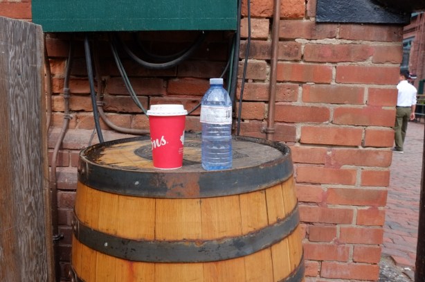 a tims coffee cup and a bottle of water on top of a barrel beside a brick building