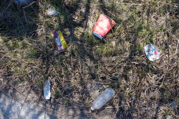 trash on the ground including an empty water bottle and a red and white tims coffee cup