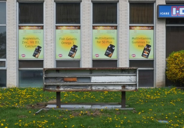 broken sign that had lights, in front of a building with ads for vitamins on the windows