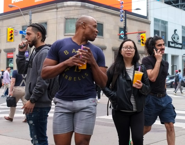 A group of people wakling, one smoking, one on phone, two with orange drinks in their hands. 