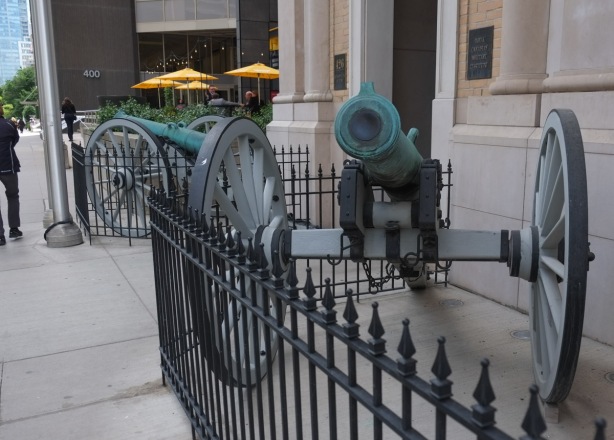 two cannons behind a black wrought iron fence by a patio with yellow umbrellas