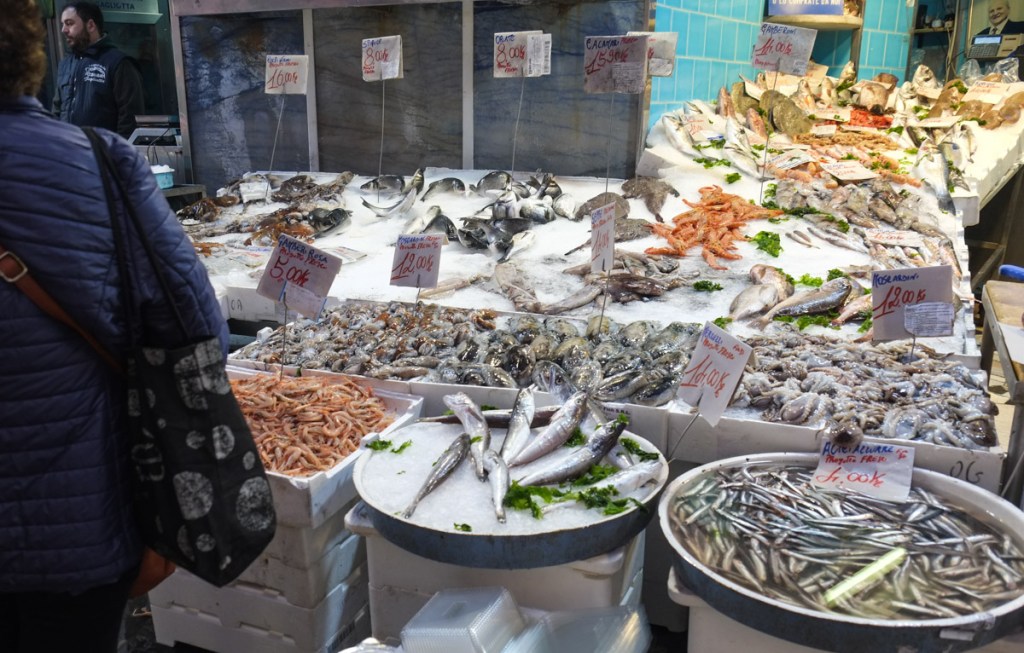 tables and boxes full of fresh fish for sale at an outdoor sidewalk market in Naples Italy