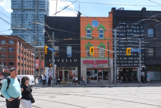 two people crossing the street by Queen West, with stores in the background, Civello, Stag Shop and another