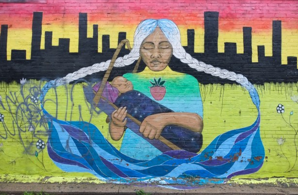 street art mural in a parkdale alley, seated woman holding baby, by chief ladybird