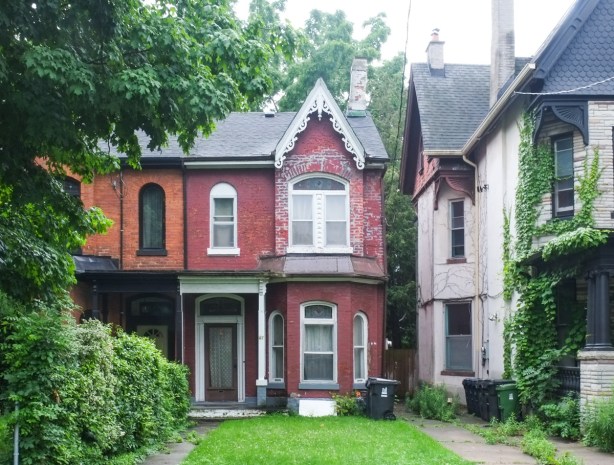maroon brick house with white gingerbread trim, attached to another brick house, orange colour, and beside a larger white brick house