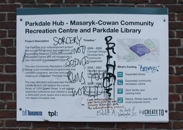graffiti, words about sorcery and science on a blue and white development notice sign for masaryk cowan community centre