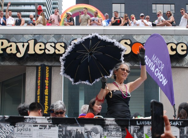 woman on a float with black parasol, pride parade, spectators on roof of payless shoe store behind her