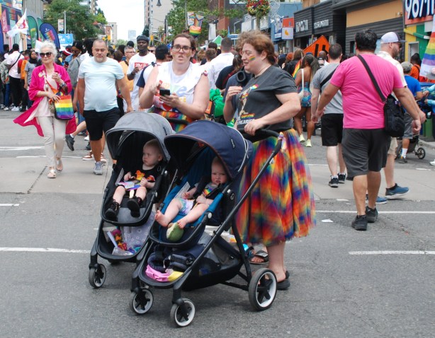 two women standing in road, crowds, both with a young child in a stroller