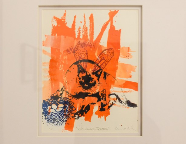 artwork on the wall of Gallery 1313, title whiskered foster, very orange, with black drawings of rabbit and cat, also in blue, a nest of eggs