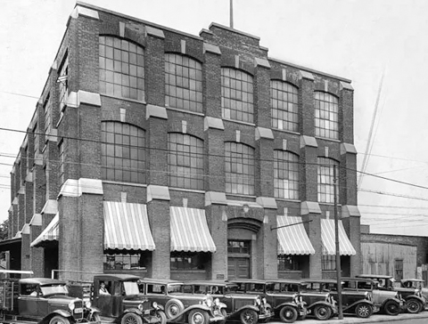black and white photo from the 1930s of Adam Beck cigar box factory, three storey brick building with cars parked in front
